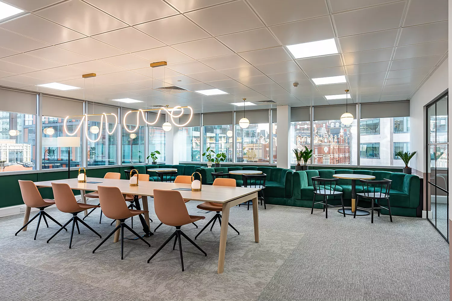 Large breakout table in front of green semi-circle booth seats. There is also grey carpet and a curved feature light.