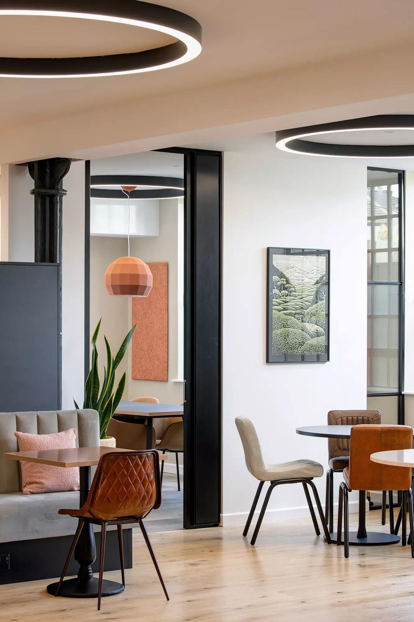 Contemporary breakout area with mixed seating styles, bold pendant lighting, indoor plants, and framed artwork, ideal for informal meetings or solo work.