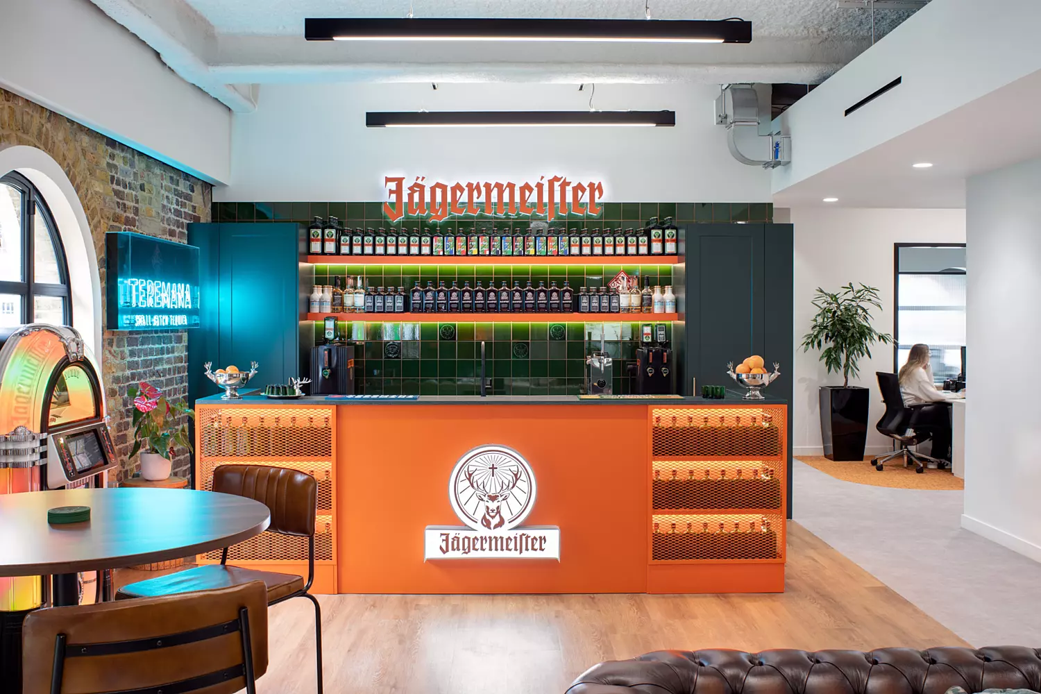 Orange kitchen bar with bottles of Jagermeister behind. Dark green wall featuring neon sign