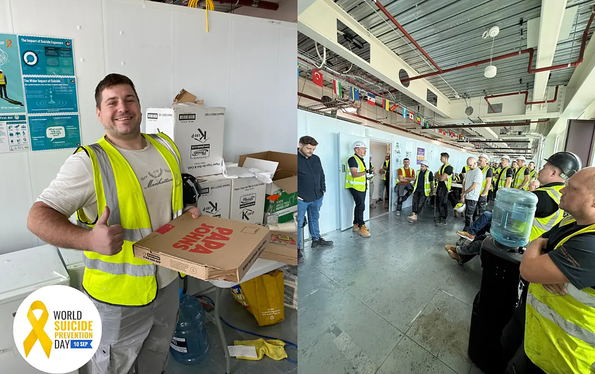 Split image showing activities on a construction site for World Suicide Prevention Day. On the left, a construction worker wearing a high-visibility vest holds several pizza boxes beside a table and stacked supplies, with safety and wellbeing posters displayed on the wall behind. On the right, a group of construction workers in high-visibility clothing and hard hats gather in a corridor while listening to a site briefing. International flags hang from the ceiling and a water dispenser is visible in the foreground. A World Suicide Prevention Day logo appears in the bottom-left corner of the image.